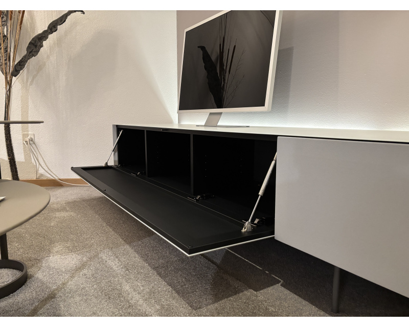 Modernes Wohnzimmer mit einem Flachbildfernseher auf einem Büromöbel mit 3 Boxenfenstern, einem eleganten weißen Schrank mit offenem Stauraum, alles auf einem grauen Teppich.